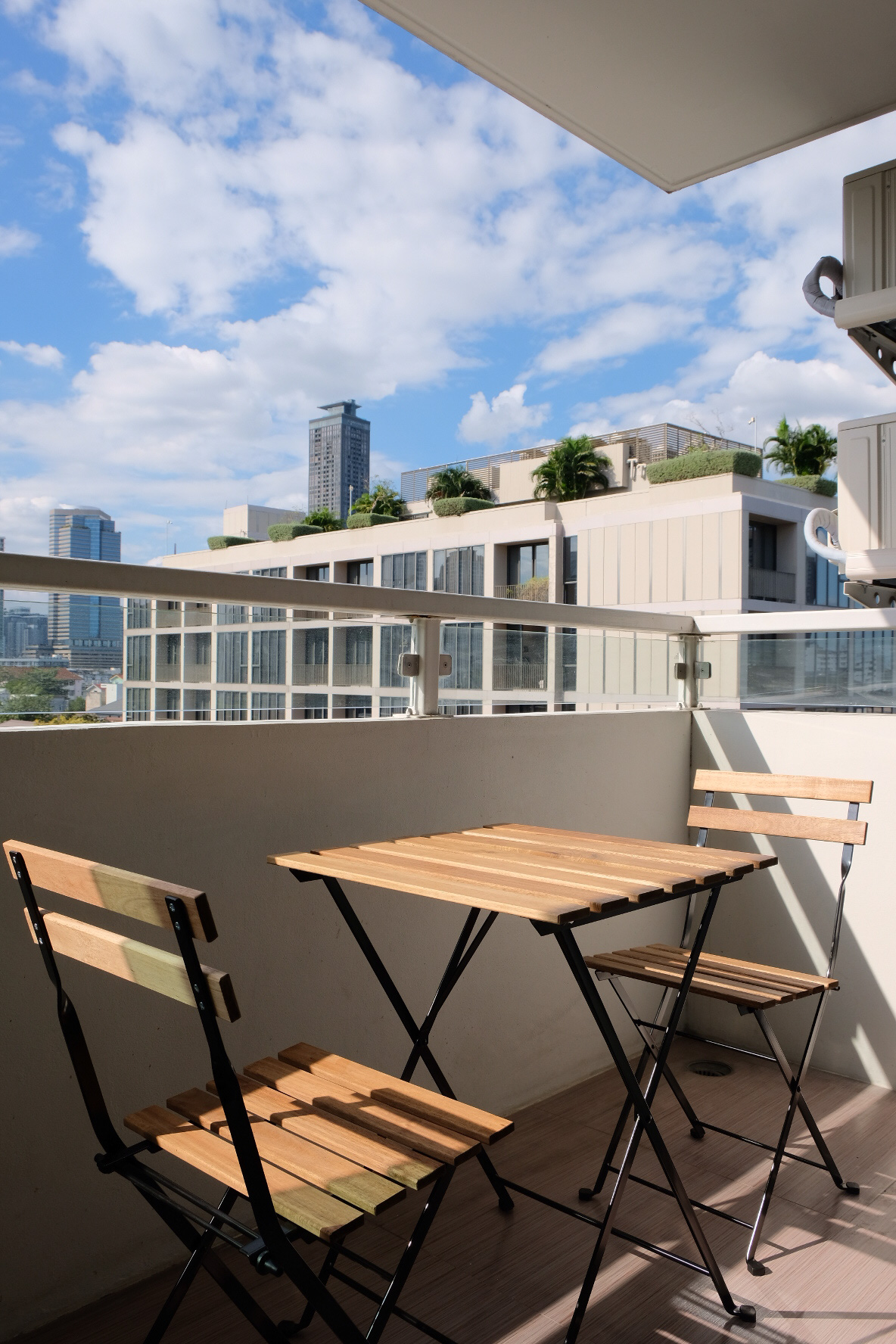 公寓 出租在Watthana, Bangkok - 阳台配木质小餐桌椅，眺望城市景与蓝天。