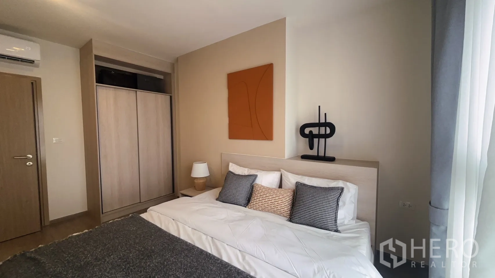 Condominium for rent in Watthana, Bangkok - Bedroom with large wardrobe, abstract wall art, and window draped with grey curtains.