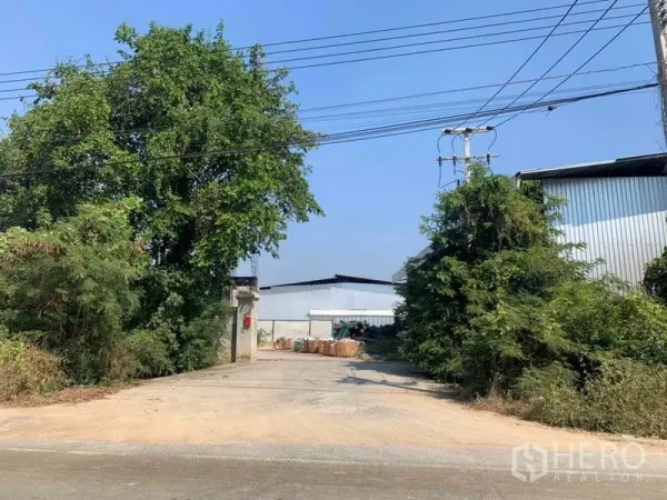 工厂 出租在Nakhon Pathom - 面向道路的厂区入口，电力线与绿化环绕。