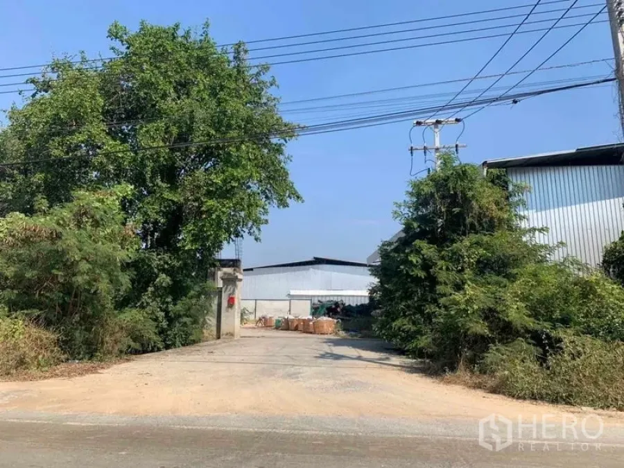 工厂 出租在Nakhon Pathom - 面向道路的厂区入口，电力线与绿化环绕。