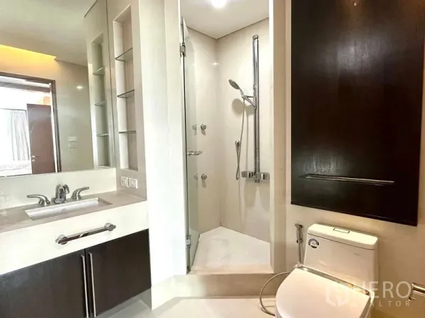 公寓 出租在Pathum Wan, Bangkok - 明亮公寓浴室，设玻璃淋浴间、洗手台与坐便器。