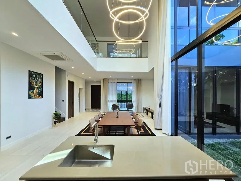 Detached House for rent in Bang Kapi, Bangkok - Open kitchen and dining room with island sink, two‑story glass wall to garden