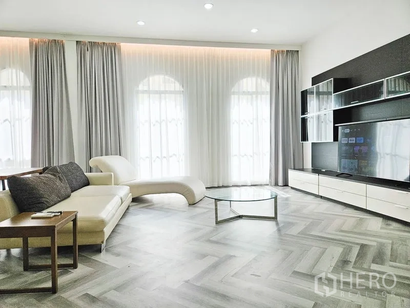 Townhouse for rent in Yan Nawa, Bangkok - Lounge with curved chaise sofa, large TV on a media wall and floor-to-ceiling curtains.