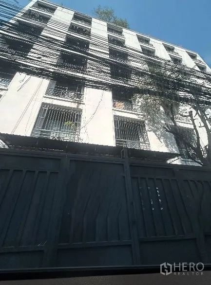 คลังสินค้า ให้เช่าในKhlong Toei, Bangkok - อาคารสไตล์โกดังหลายชั้น มีกริลเหล็ก ประตูรั้วสูง และสายไฟเหนือศีรษะ ในย่านคลองเตย ท้องฟ้าแจ่มใส