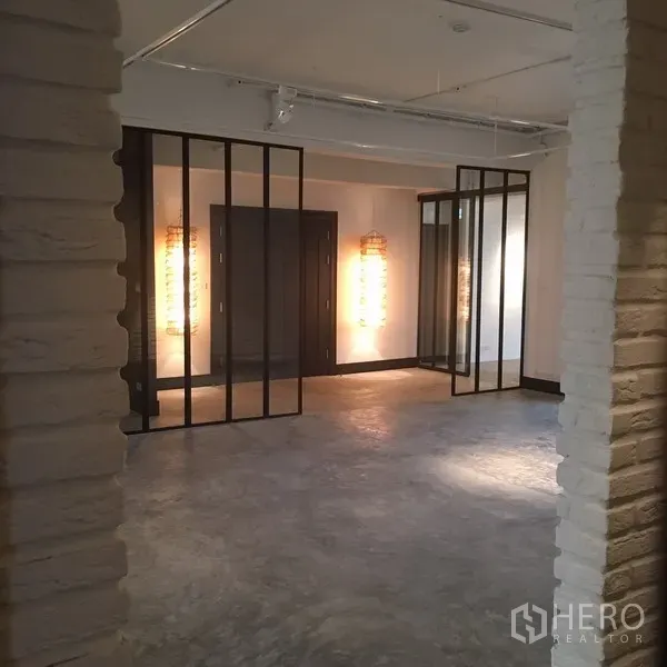 คอนโด ให้เช่าในWatthana, Bangkok - พื้นที่นั่งเล่นโล่ง ปูนขัดมัน พร้อมฉากกั้นกระจกกรอบเหล็กและโคมไฟตกแต่ง.