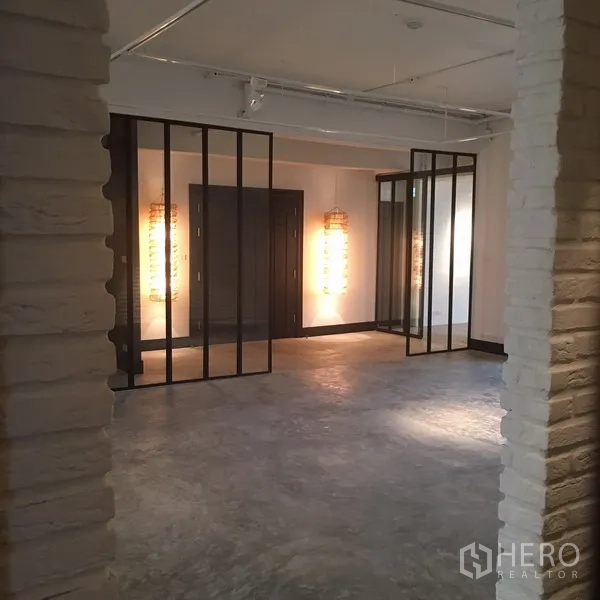 คอนโด ให้เช่าในWatthana, Bangkok - พื้นที่นั่งเล่นโล่ง ปูนขัดมัน พร้อมฉากกั้นกระจกกรอบเหล็กและโคมไฟตกแต่ง.