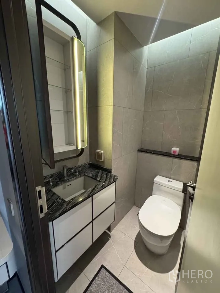 Condominium for rent in Watthana, Bangkok - Compact powder room with illuminated mirror, vanity and toilet.