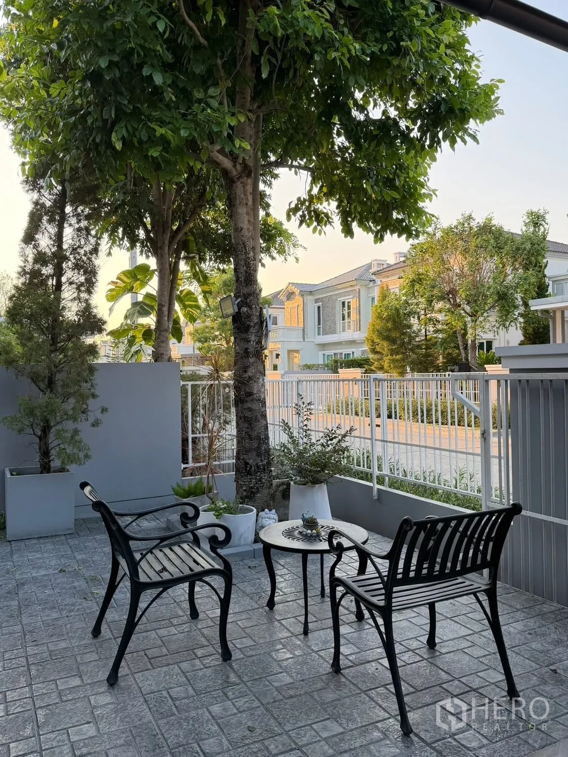 Semi-detached House for rent in Prawet, Bangkok - Shaded front patio with two metal benches and a round table beneath mature trees.