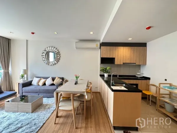 Condominium for rent in Watthana, Bangkok - Bright open-plan living room with dining table and wood-tone kitchen with black countertops in a Phra Khanong condo.