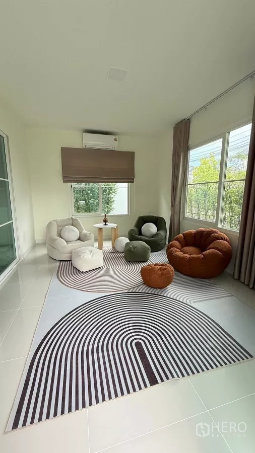 บ้าน ให้เช่าในBang Phli, Samut Prakan - ห้องอเนกประสงค์สว่างด้วยเก้าอี้นั่งสบาย พรมลายกราฟิก และวิวสวน.