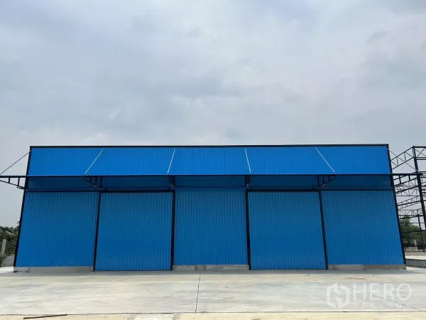 Warehouse for rent in Khlong Toei, Bangkok - Blue metal-clad warehouse exterior with three large sliding doors and a wide concrete forecourt.