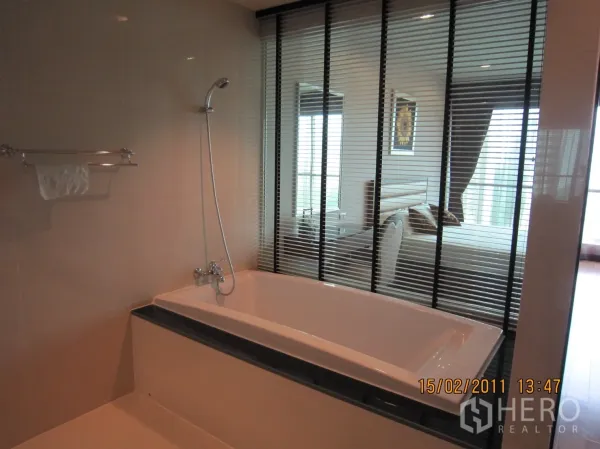 คอนโด ให้เช่าหรือขายในPathum Wan, Bangkok - อ่างอาบน้ำแบบบิ้วท์อินพร้อมฝักบัวถัดจากหน้าต่างบานมู่ลี่ที่มองเข้าห้องนอน