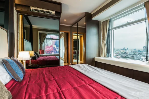 Condominium for rent in Ratchathewi, Bangkok - Corner bedroom with red duvet, mirrored wardrobe and a large city-view window in a Ratchathewi condo.