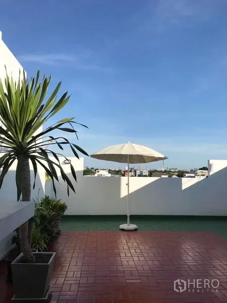 Townhouse for sale in Suan Luang, Bangkok - Rooftop terrace with red tiles, potted palms and a parasol overlooking the city.