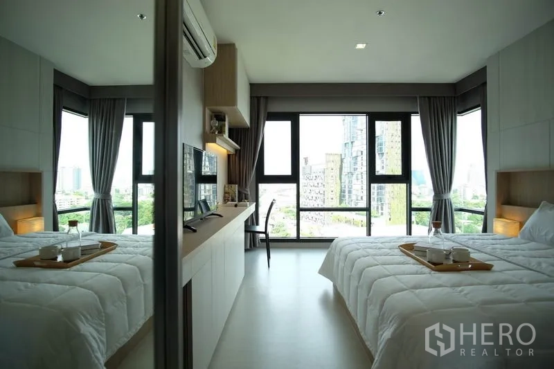 Condominium for rent in Khlong Toei, Bangkok - Wide view of bedroom with mirrored wardrobe reflecting bed and full-height windows.