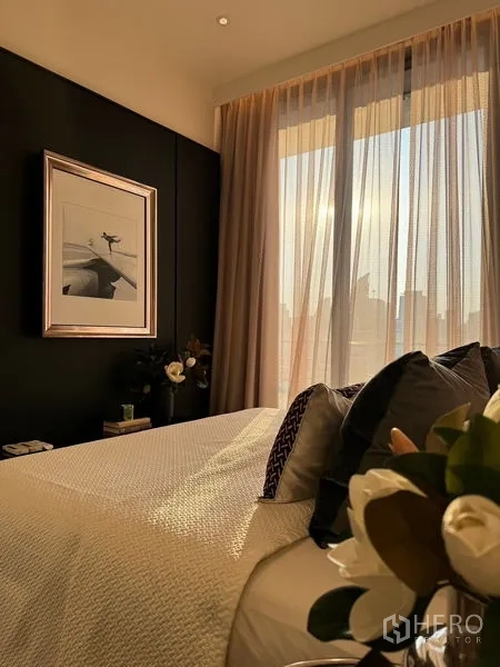 Condominium for sale in Watthana, Bangkok - Bedroom with black feature wall, framed art and sunset city view filtered by sheer curtains.