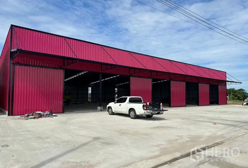Warehouse for rent in Ban Pho, Chachoengsao - Exterior perspective of the red metal warehouse blocks with spacious concrete yard for truck parking.