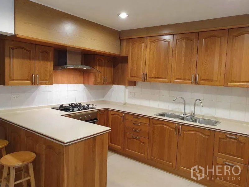 独立式住宅 出租在Phra Khanong, Bangkok - U型厨房，整排木质橱柜，燃气灶、抽油烟机与双水槽。