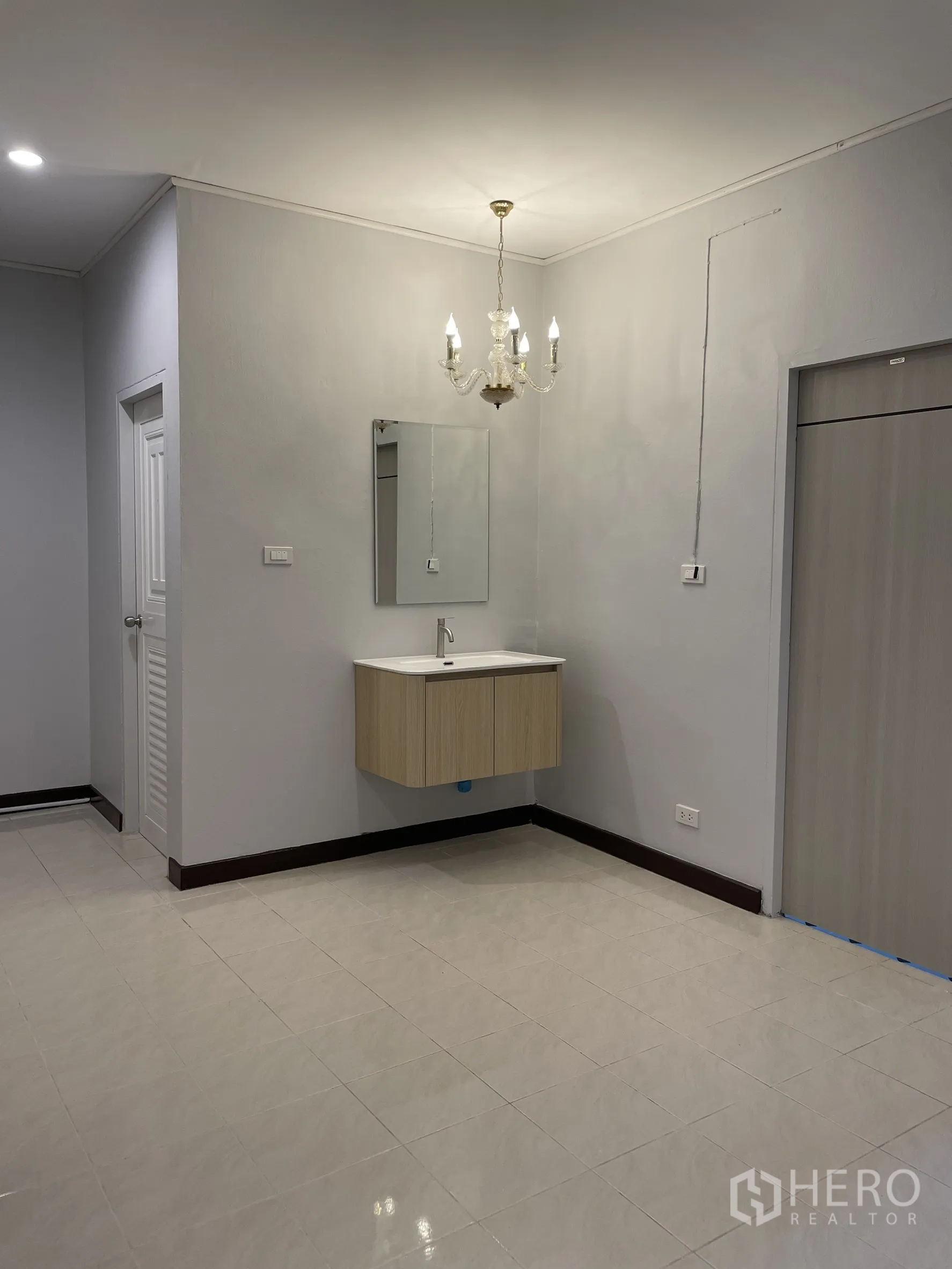 Shophouse for rent in Bang Kapi, Bangkok - Close view of chandelier above floating vanity and mirror in a neutral tiled space.