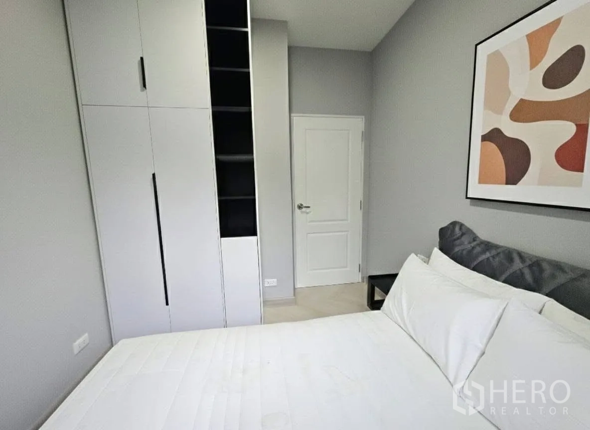 Detached House for rent or sale in Bang Phli, Samut Prakan - Cozy bedroom with white bedding, abstract wall art, and a tall built-in wardrobe with open shelving.