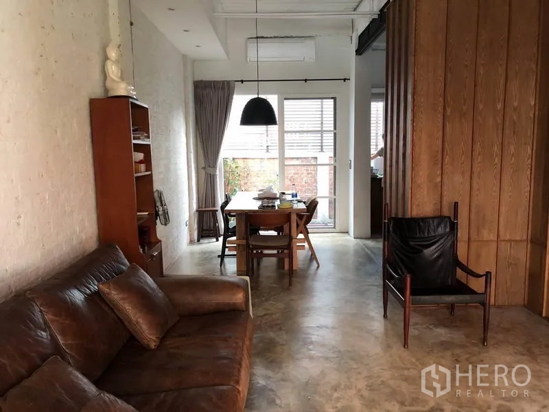 ทาวน์เฮาส์ ขายในWang Thonglang, Bangkok - พื้นที่นั่งเล่นและรับประทานอาหารแบบโอเพ่นสเปซ โซฟาหนัง โคมแขวน และประตูกระจกออกสู่ลานบ้าน