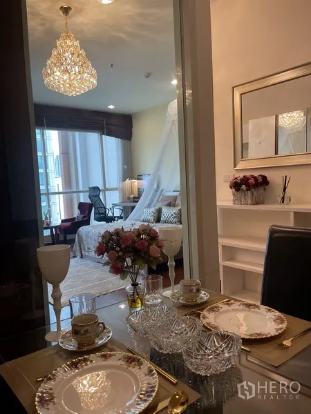 คอนโด ให้เช่าหรือขายในPathum Wan, Bangkok - มุมรับประทานอาหารโต๊ะกระจกพร้อมโคมระย้า มองเห็นห้องนอนสว่างในคอนโดกรุงเทพฯ
