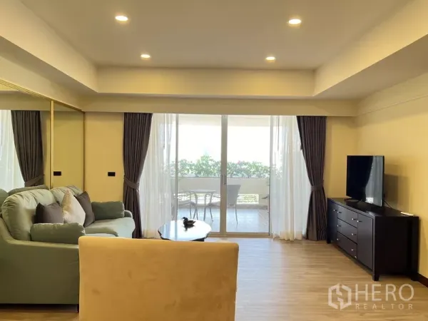 คอนโด ให้เช่าในKhlong Toei, Bangkok - ห้องนั่งเล่นสว่าง โซฟา ตู้วางทีวี และประตูกระจกบานเลื่อนเปิดสู่ระเบียงมีต้นไม้พร้อมชุดนั่ง