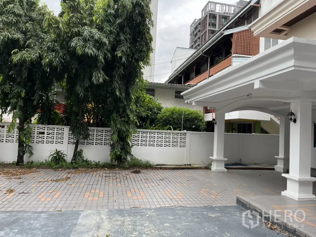 บ้าน ให้เช่าในWatthana, Bangkok - ลานกว้างหน้าบ้าน ปูพื้นกระเบื้อง กำแพงรั้วสีขาว และพื้นที่สีเขียวข้างที่จอดรถ.