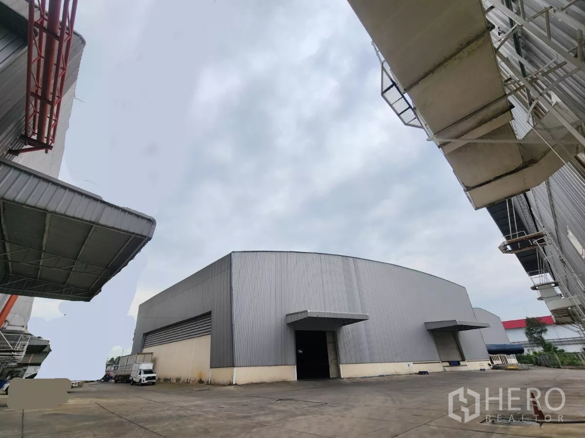 Warehouse for rent in Mueang Samut Sakhon, Samut Sakhon - Exterior view of a large steel-clad warehouse with loading canopies and a wide concrete yard in Samut Sakhon Industrial Estate.