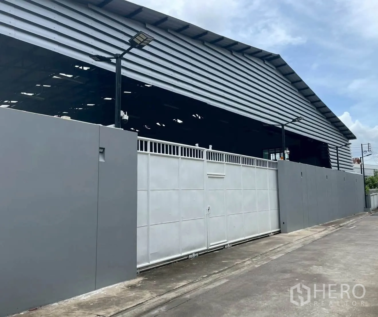 โกดัง for rent in Taling Chan, Bangkok - มุมมองด้านหน้าถนนของโกดังพร้อมรั้วสูง ประตูรั้ว และไฟส่องสว่างภายนอก.