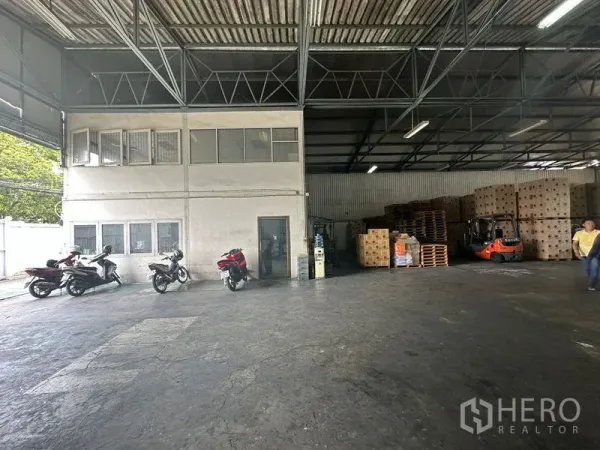 Warehouse for rent in Suan Luang, Bangkok - Interior with two-storey office pod, forklifts and stacked pallets under a high roof.
