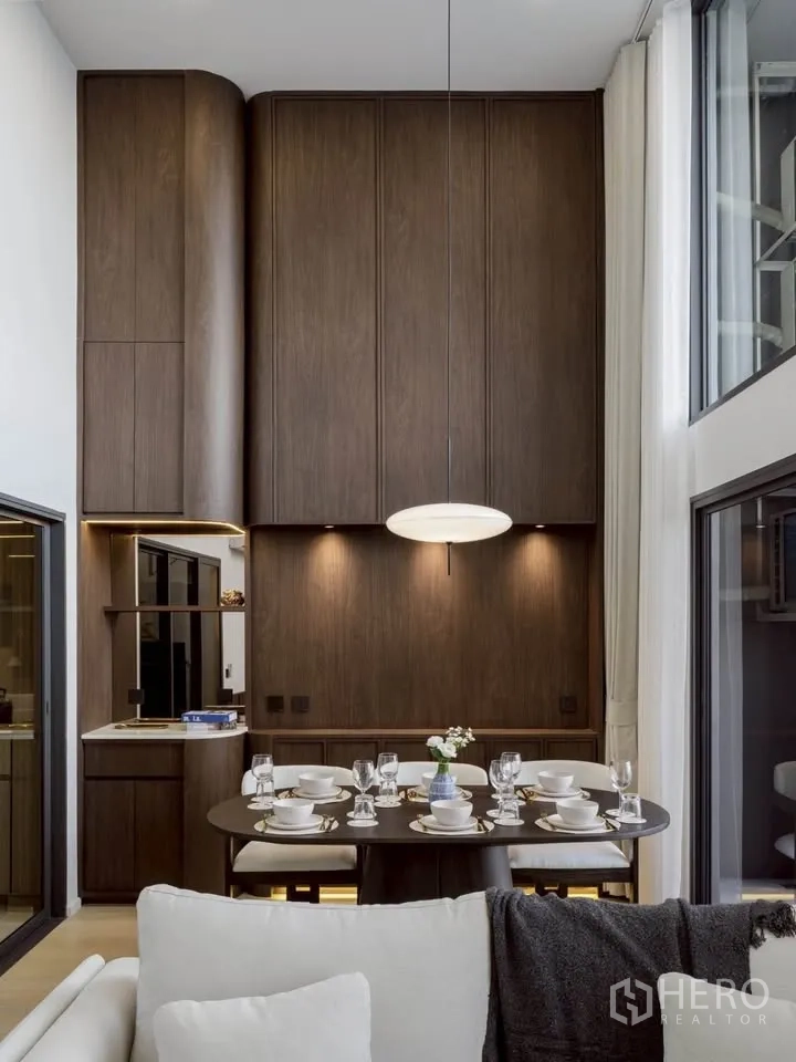 Condominium for rent in Khlong Toei, Bangkok - Dining zone with soaring wood-paneled feature wall and modern pendant lamp.