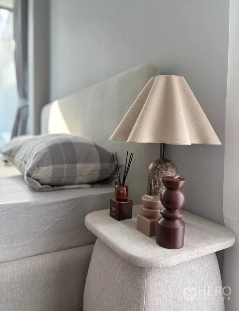 Detached House for rent in Suan Luang, Bangkok - Close-up of bedside table with decorative lamp and accessories beside an upholstered headboard.