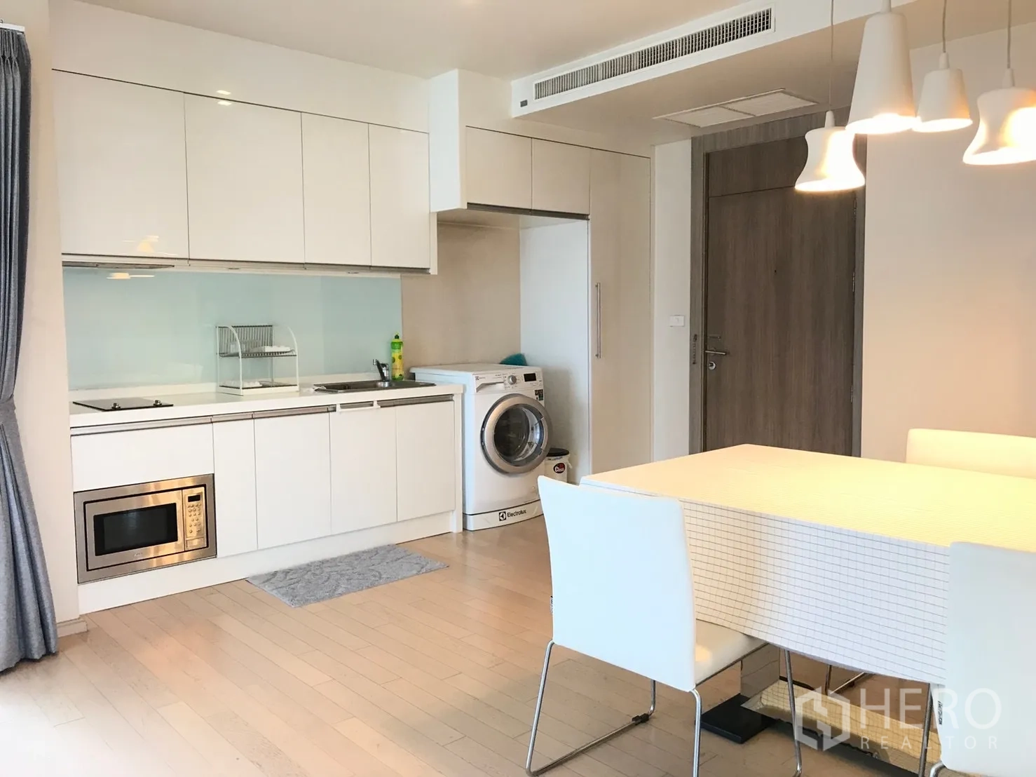 公寓 出租在Watthana, Bangkok - 现代白色一字型厨房，内置灶台、微波炉、橱柜、洗衣机与餐桌。