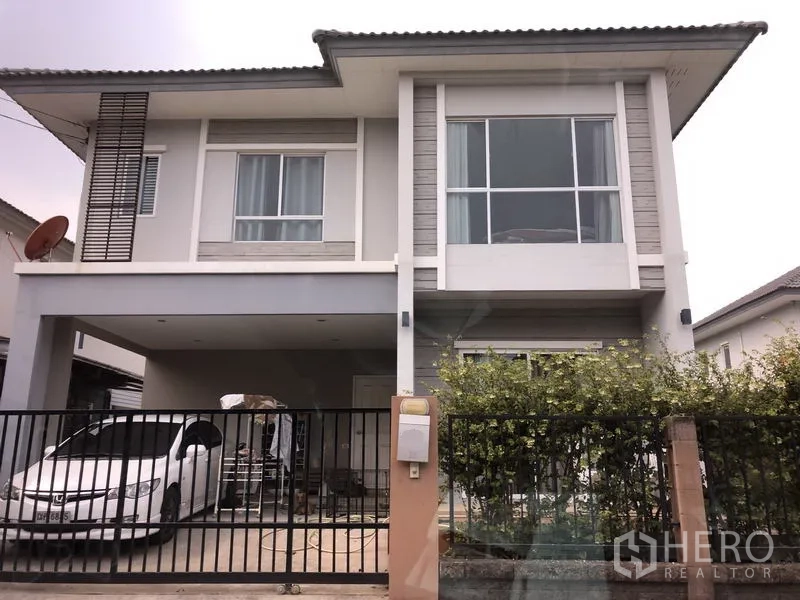 Detached House for sale in Saphan Sung, Bangkok - Two-storey modern detached house exterior with large windows, covered double carport, black metal fence and hedge.