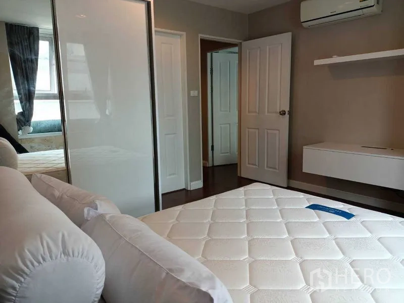 Condominium for rent or sale in Huai Khwang, Bangkok - Bedroom with air conditioner, built-in shelves and sliding wardrobe doors.
