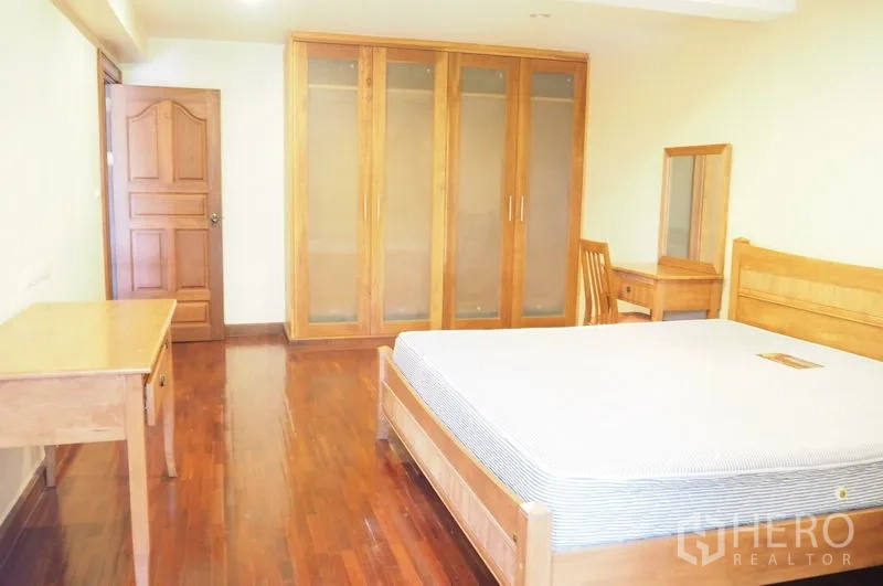 Condominium for rent in Pathum Wan, Bangkok - Large bedroom featuring built-in wardrobes with glass fronts and wood floors