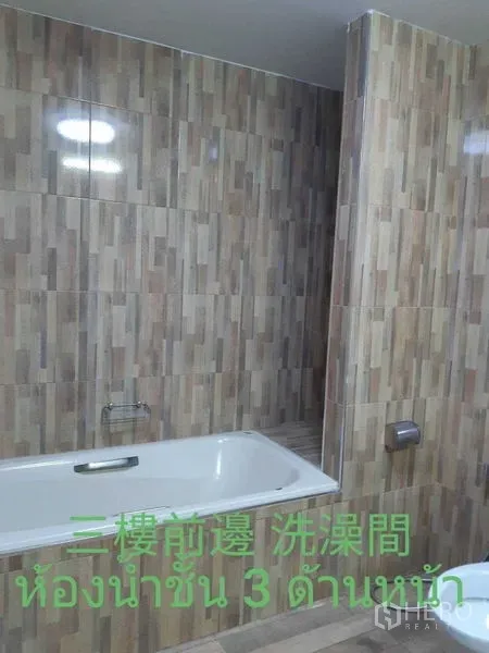 Townhouse for rent in Watthana, Bangkok - Bathroom with bathtub and wood‑pattern tiled walls.