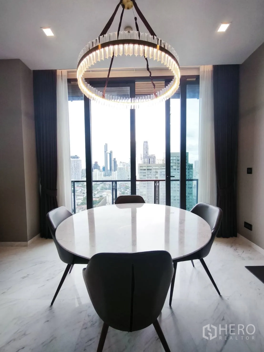 Condominium for rent in Watthana, Bangkok - Dining area with ring chandelier and city-view windows.