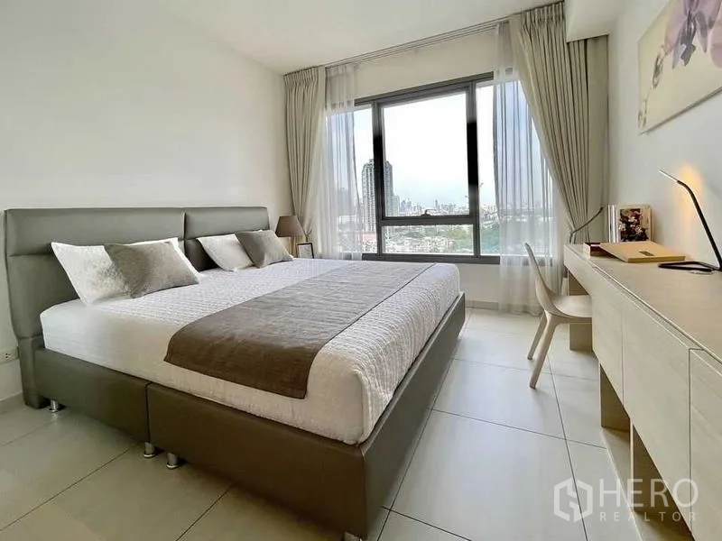 คอนโด ให้เช่า - ห้องนอนสว่าง เตียงคิงไซซ์ โต๊ะทำงาน และหน้าต่างบานใหญ่เห็นวิวกรุงเทพฯ