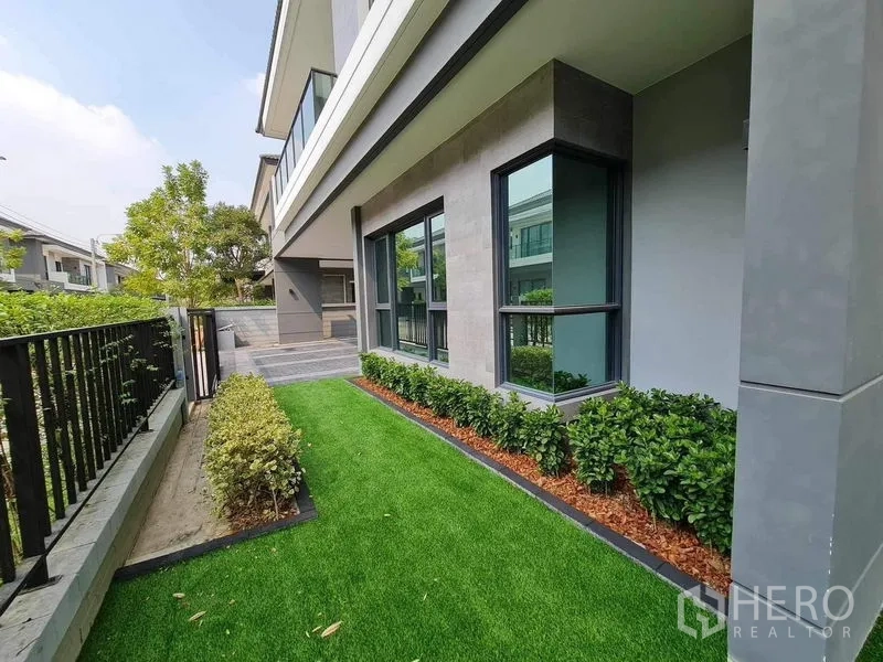 Detached House for rent or sale in Bang Phli, Samut Prakan - Side garden along house facade with shrubs and large windows.