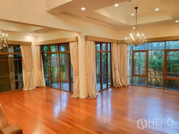 独立式住宅 出租在Watthana, Bangkok - 挑高客厅，水晶吊灯、实木地板与落地窗，景观绿意盎然。
