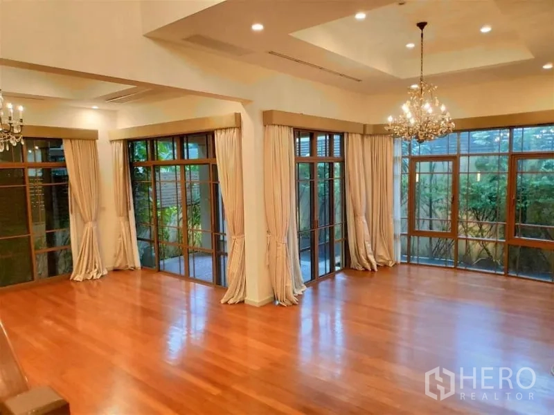 独立式住宅 出租在Watthana, Bangkok - 挑高客厅，水晶吊灯、实木地板与落地窗，景观绿意盎然。