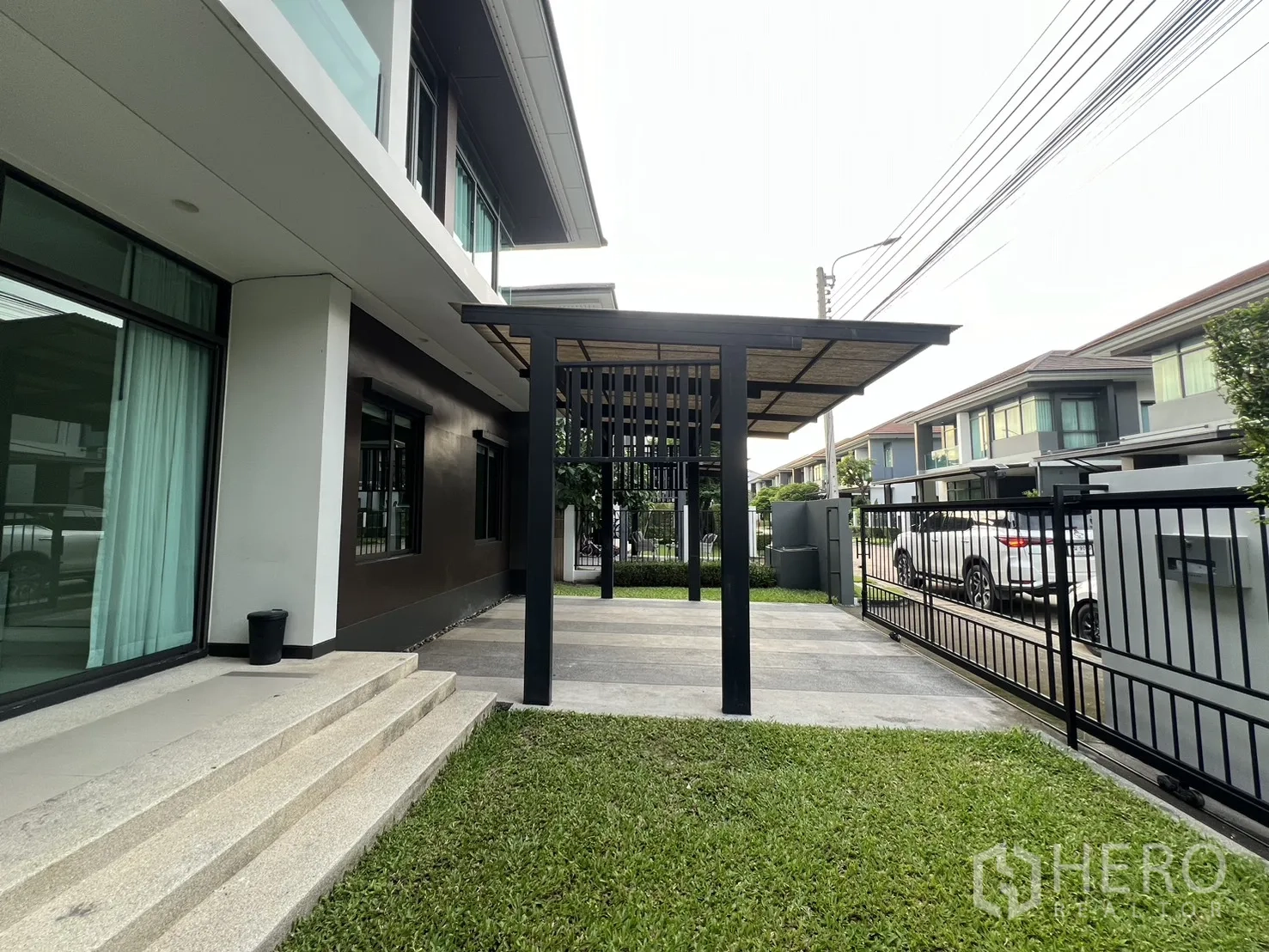 บ้าน ให้เช่าในBang Kapi, Bangkok - สนามหญ้าหน้าบ้านกับบันไดสู่ประตูกระจกบานเลื่อนและกันสาดเหล็ก