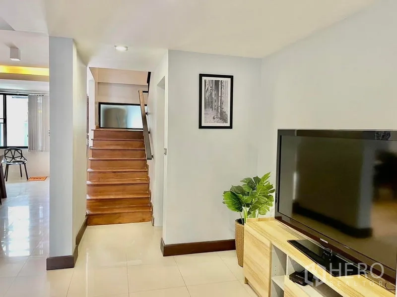 Townhouse for rent in Khlong Toei, Bangkok - Hallway with wooden staircase, TV console, and glossy tiled floors.