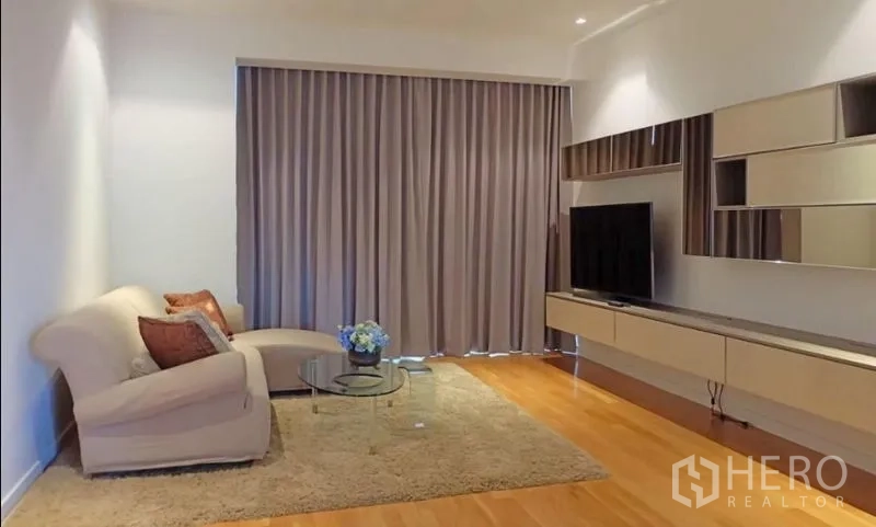 Condominium for rent or sale in Yan Nawa, Bangkok - Modern living room with sofa, TV wall unit and full-length curtains.