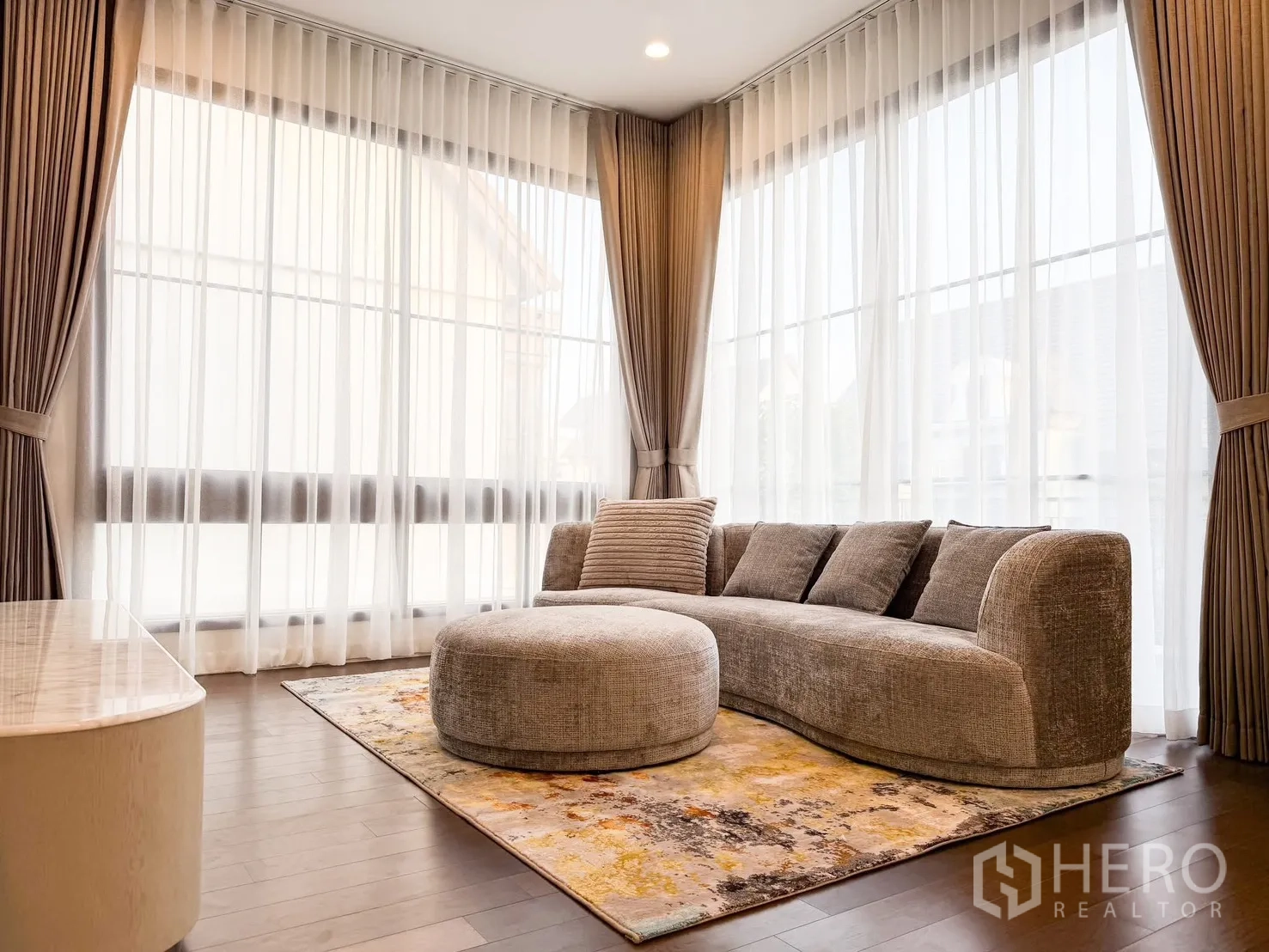 บ้านเดี่ยว for rent in Bang Khen, Bangkok - ห้องนั่งเล่นชั้นบน โซฟาทรงโค้งพร้อมออตโตมัน และหน้าต่างมุมผ้าม่านโปร่ง.