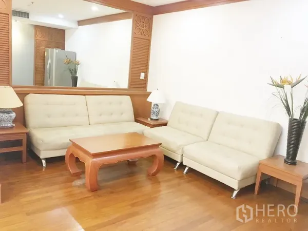 公寓 出租在Pathum Wan, Bangkok - 舒适客厅，米色沙发、木质茶几和大幅墙面镜。