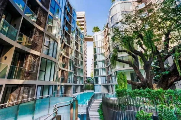 Condominium for rent - Exterior between two curved glass buildings with a sky bridge and resort-style pool set among lush greenery.