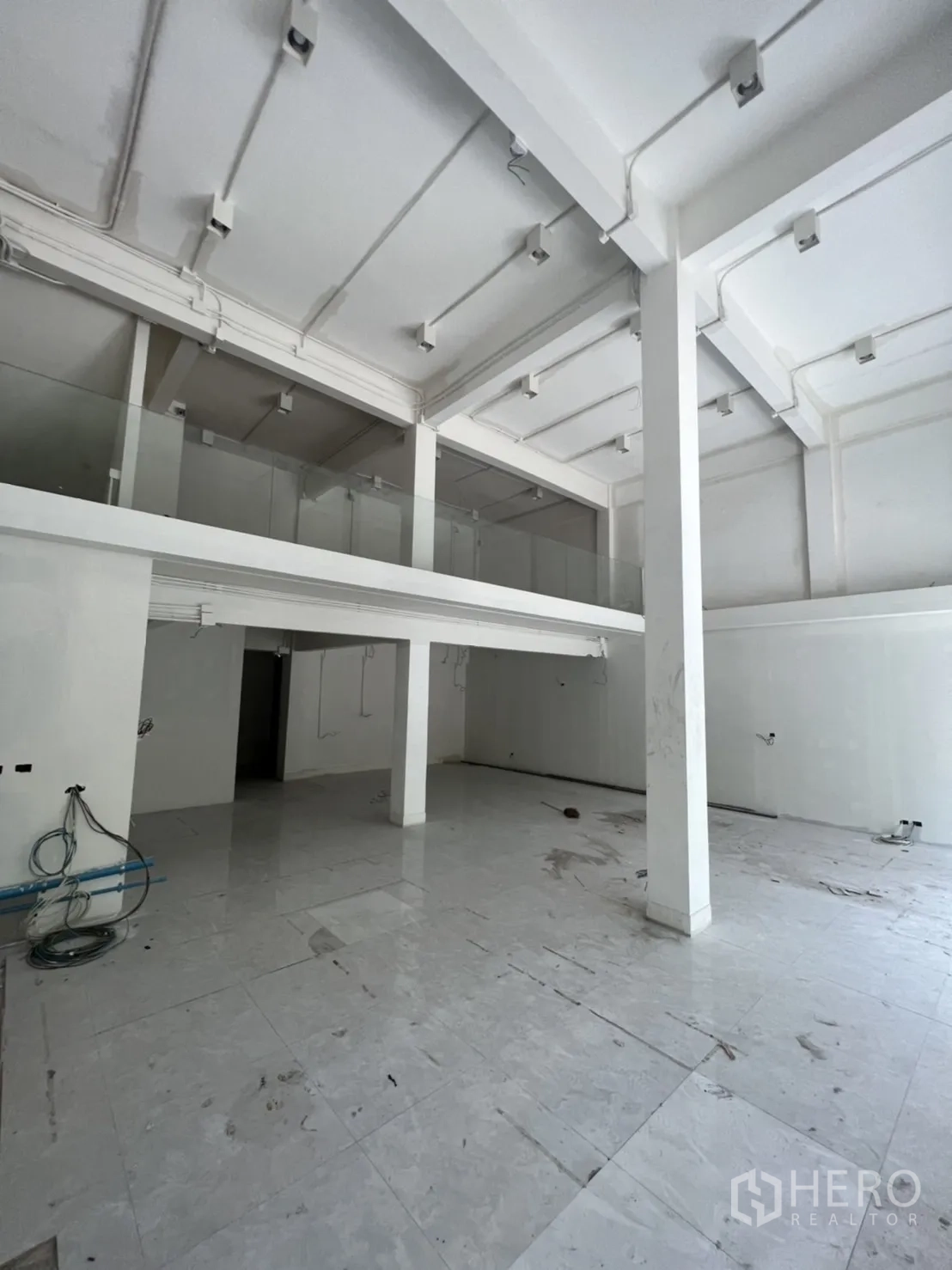 店屋 出租在Watthana, Bangkok - 店屋一层挑高空间，白色立柱、夹层与瓷砖地面。